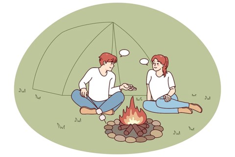 Happy man and woman sitting near campfire in forest. Smiling couple relax at wood camp near fire