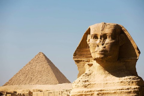 A closeup of the head of the Great Sphinx and the Pyramid of Menkaure in the distance in Giza,