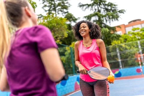 Happy pair of multi-ethnic women playing pickelball in an outdoor court