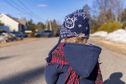 Back view of infant in winter clothing with thick coat, and blue wooly hat on a cold sunny day with