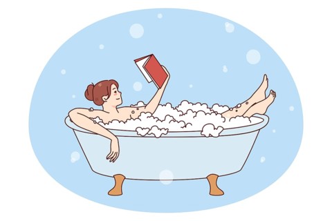 Happy young woman relaxing in bathtub with foam reading book. Calm girl rest in bath with bubbles