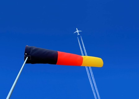 A passenger plane with vapour trails high in the blue sky and a german windsock