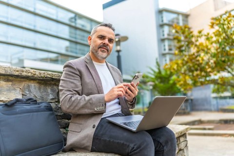 Mature male digital nomad working with laptop and mobile phone outdoors in the city