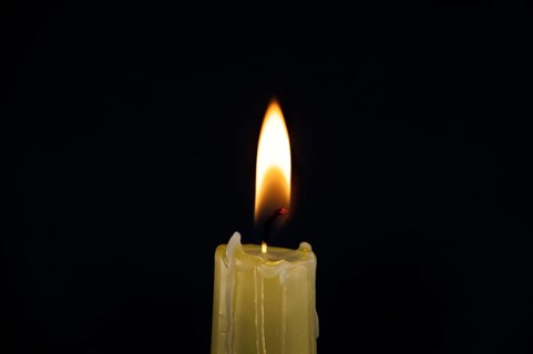 Burning yellow wax candle contrasting with the dark background, candle's gentle flame suggesting of