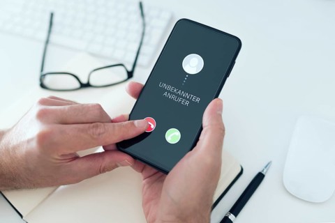 close-up view of person rejecting call from unknown number with text UNBEKANNTER ANRUFER, German