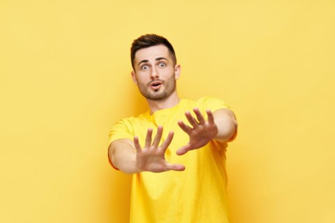 Young displeased man making stop gesture sign say no isolated on yellow background. Negative