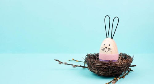 Easter bunny or rabbit sitting in a bird nest, willow branches, wooden egg, spring holiday, brown