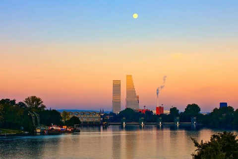 River landscape at sunset with skyscrapers and full moon. The scene contains natural and industrial