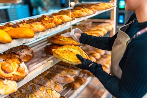 Close-up of hands of a woman using gloves to arrange artisan bread in shop shelf