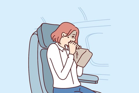 Woman passenger of airplane suffers from aerophobia and breathes into paper bag, sitting in