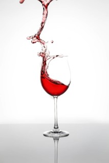 Red wine splashes from an elegant wine glass against a white background, wine splashes