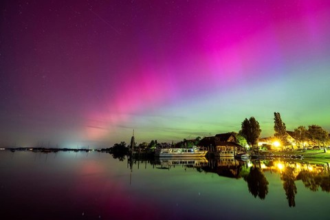 Calm lake with vivid auroras reflected next to illuminated buildings, harbour, Allensbach, Lake