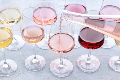 Rose wine pour into a glass at a tasting. Rose, red, and white wine, drinks on a table at a winery.