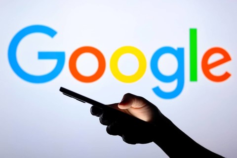 In this photo illustration the Google logo seen in the background of a silhouette hand holding a