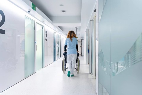 Rear view of nurse pushing a wheelchair along the hospital with a mature woman sitting on it