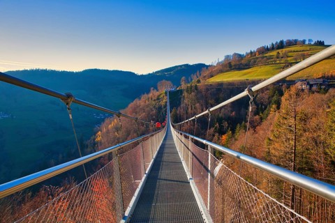 A suspension bridge leads over autumnal landscapes with hills in the background, Black Forest Line,