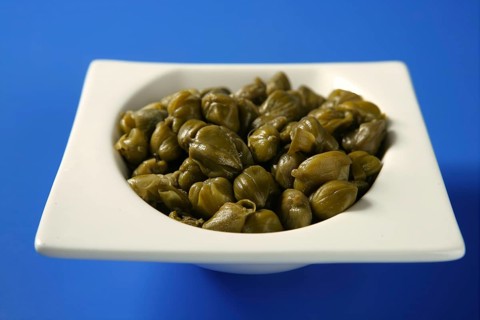 Capers with vinegar snack on a white plate, blue background