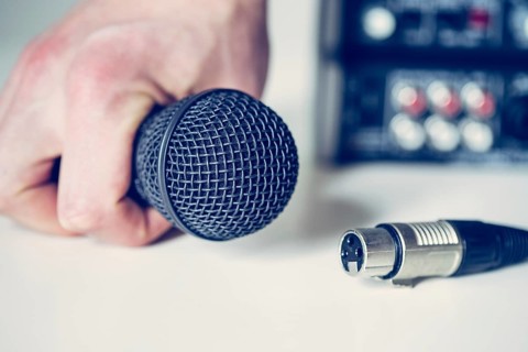 Close up picture of holding in hand microphone and audio cable, mixer in the blurry background