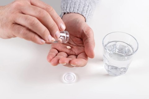 Male hands with bottle of pills and glass of water over white table