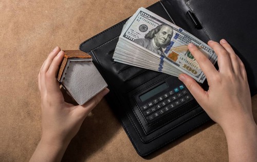 Hand holding house beside American dollar banknotes and globe