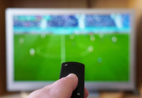 hand pointing remote control at tv set with soccer or football match