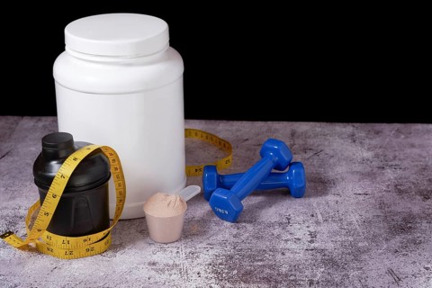 Whey protein powder, shaker, measuring tape and dumbbells on black background and copy space