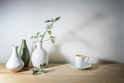 Pale still life with three vases in white and green, a sage leaf branch with shadow and a coffee
