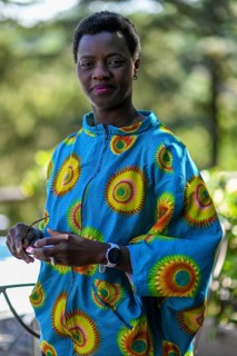 Young adult afro hair diverse model in traditional attire smiles softly while holding sunglasses