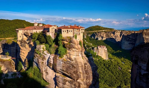 Clifftop Varlaam monastery lit by evening sunlight in Meteora, Greece in typical Meteora landscape