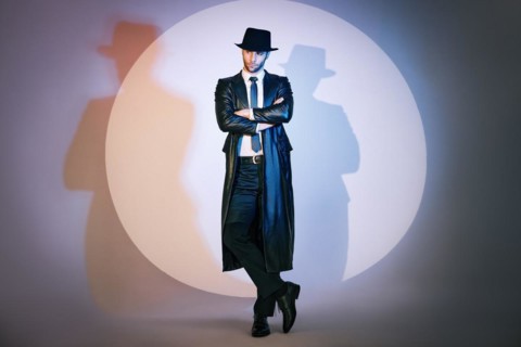 Full length portrait of confident handsome man in black coat and hat with crossed arms posing on