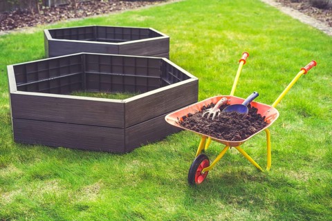 Garden barrow with soil and empty raised beds on grass prepared for filling with soil. Urban