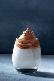 Dalgona cold coffee in a glass on a dark blue background with copy space. Trendy Korean milk shake