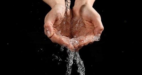 Hands of Woman and Water against Black Background
