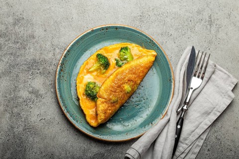 Healthy vegetarian egg omelette with green broccoli folded in half served on plate with fork and