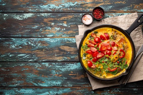 Healthy frittata in cast iron pan with fried beaten eggs and seasonal vegetables on rustic wooden