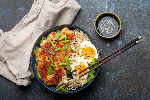 Asian noodles ramen soup with deep fried panko chicken fillet and boiled eggs in ceramic bowl with