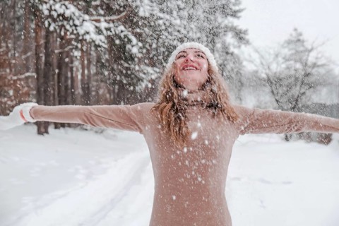 Christmas, holidays and season concept. Young happy woman blowing snow in the winter forest nature.