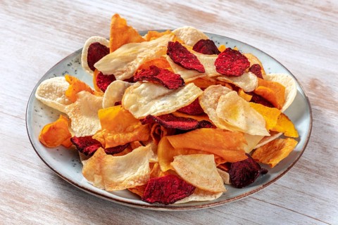 Vegetable chips on a plate, a healthy vegan snack on a wooden background