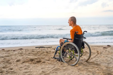 Portrait a disabled person on his back in a wheelchair on the beach with open arms enjoying the