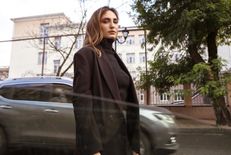 Car window view on young stylish woman in black trendy clothes walking city street on autumn day,