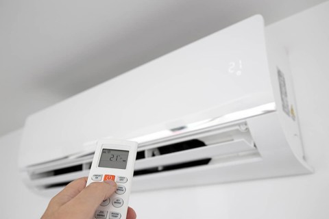 Hand operating a Remote control of a Domestic Air conditioner unit mounted on wall