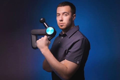 Portrait of a confident professional masseur with a percussion massager in his hands. Low key, blue