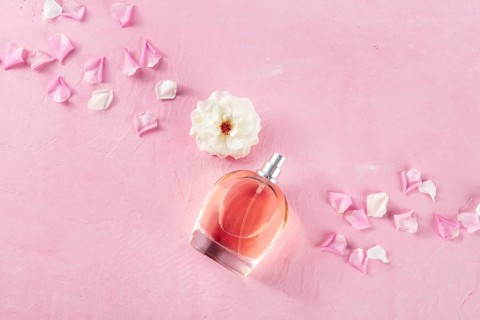 Rose fragrance bottle, a luxury product, shot from the top on a pink background with fresh flowers