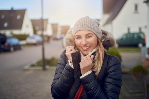 Smiling happy middle-aged woman standing outdoors on a cold winter day in a warm jacket and knitted