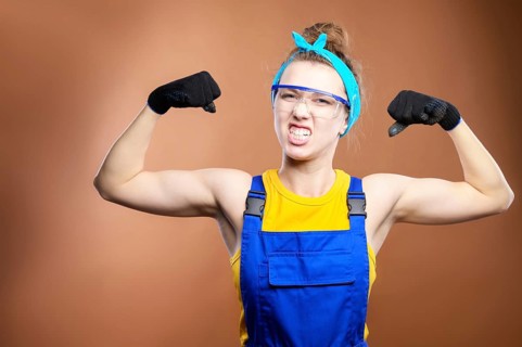 Young beautiful caucasian woman repairman worker with blue eyes in uniform showing arm muscles,