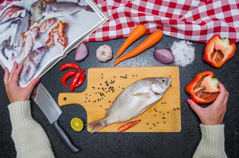 Preparing a gastronomic dish of roasted corvina, Young woman consulted the cookbook while preparing