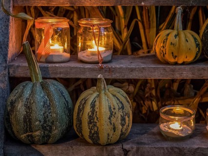 Various pumpkins and candles in jars on a wooden shelf as a cosy Halloween decoration at night,
