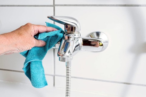 Cleaning a bathtub faucet with a blue microfiber cloth to remove limescale stains from hard calcium