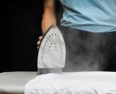 Male person using a steaming hot iron over a white shirt