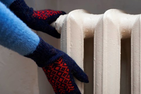 Human warming up hands in mittens near Hot Water Radiator. Space for text